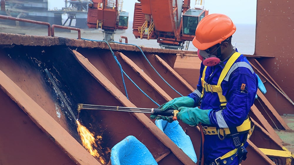 A man in blue shirt and orange safety gear working on a ship, ensuring safety and maintenance.