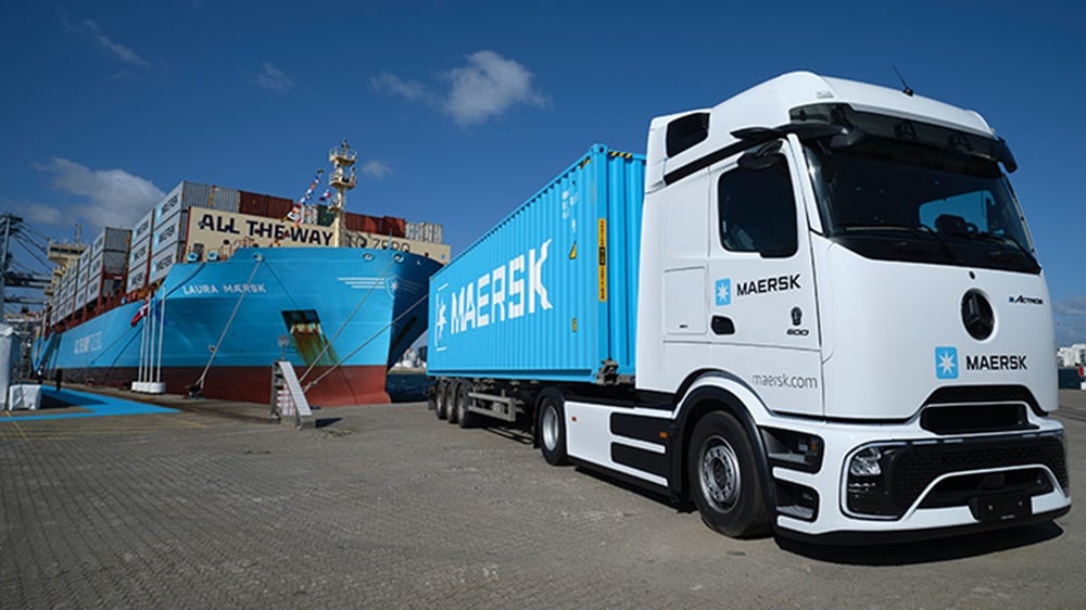 港口上，装有集装箱的东升国际电动卡车停靠在 Laura Maersk 号货轮附近，展示符合可持续发展的多式联运